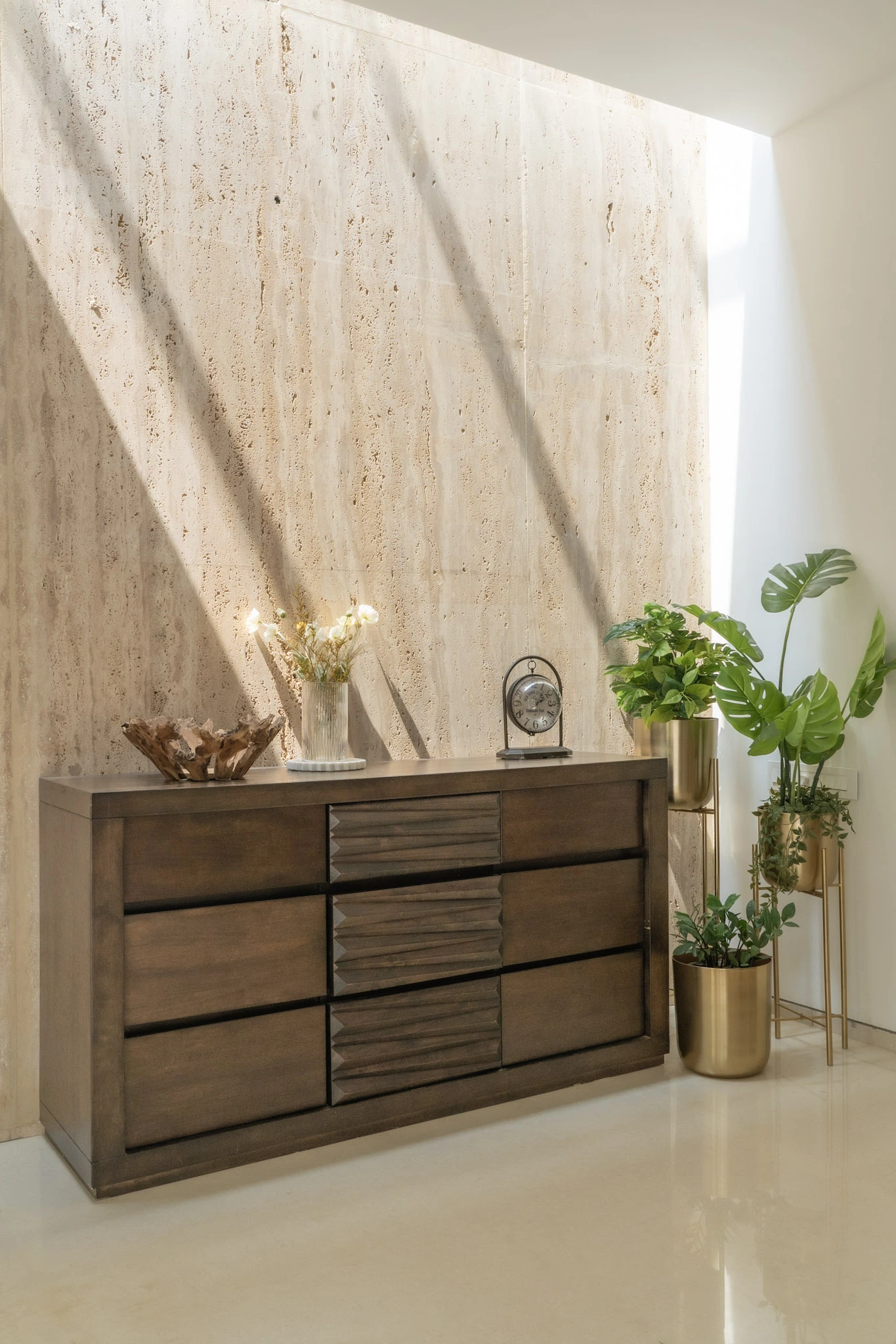 Luxury villa interior with wooden chest of drawers, marble feature wall, indoor plants, and natural sunlight
