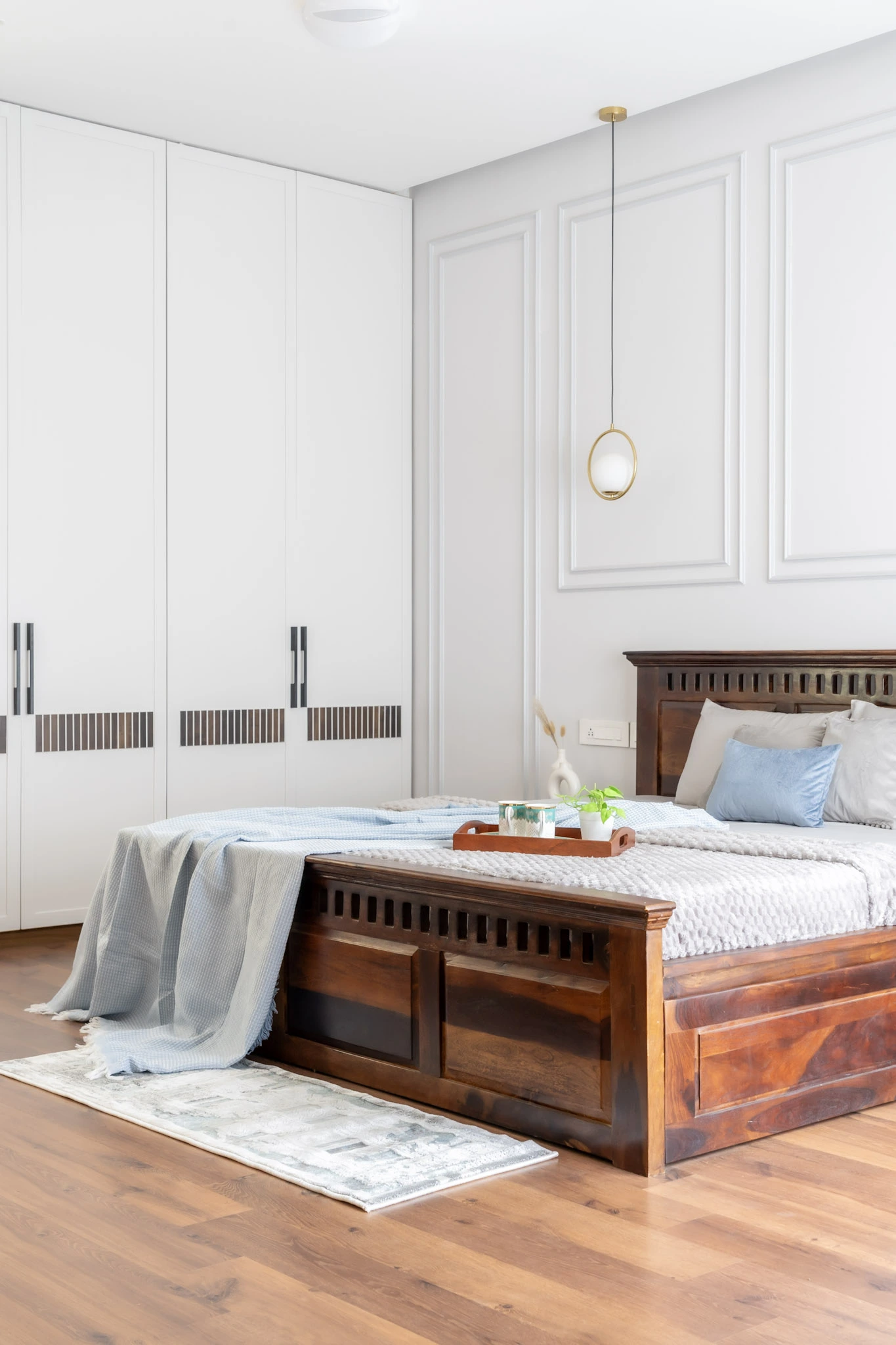 Modern master bedroom interior with wooden bed, white wardrobes, pendant lighting, and wooden flooring