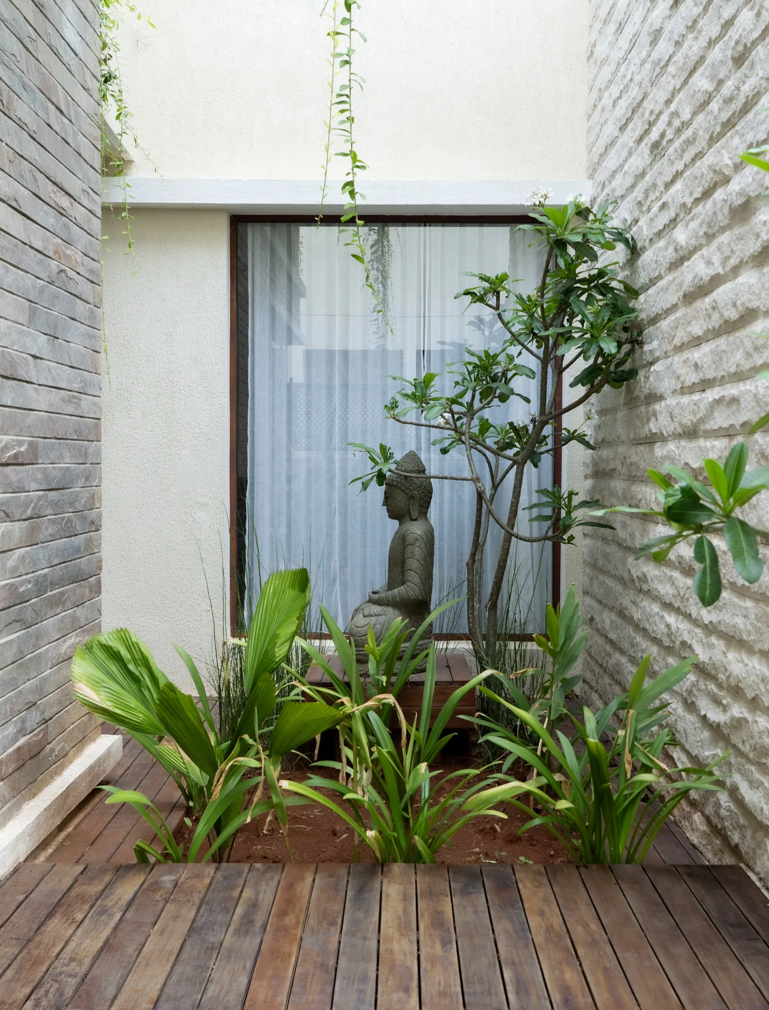 Modern villa courtyard landscape with Buddha statue, indoor garden, natural stone wall, and wooden deck design in Bangalore home