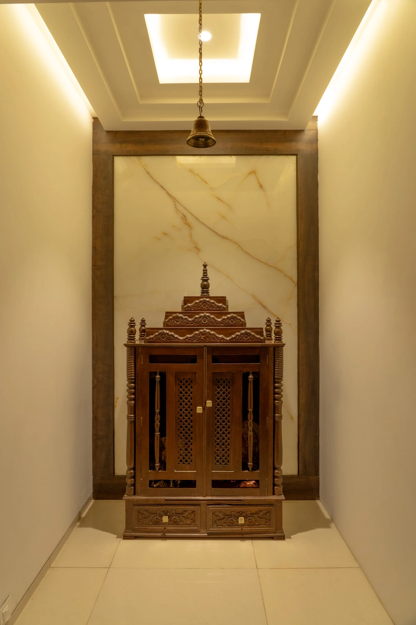 Traditional wooden pooja room design with marble backdrop and warm ceiling lighting