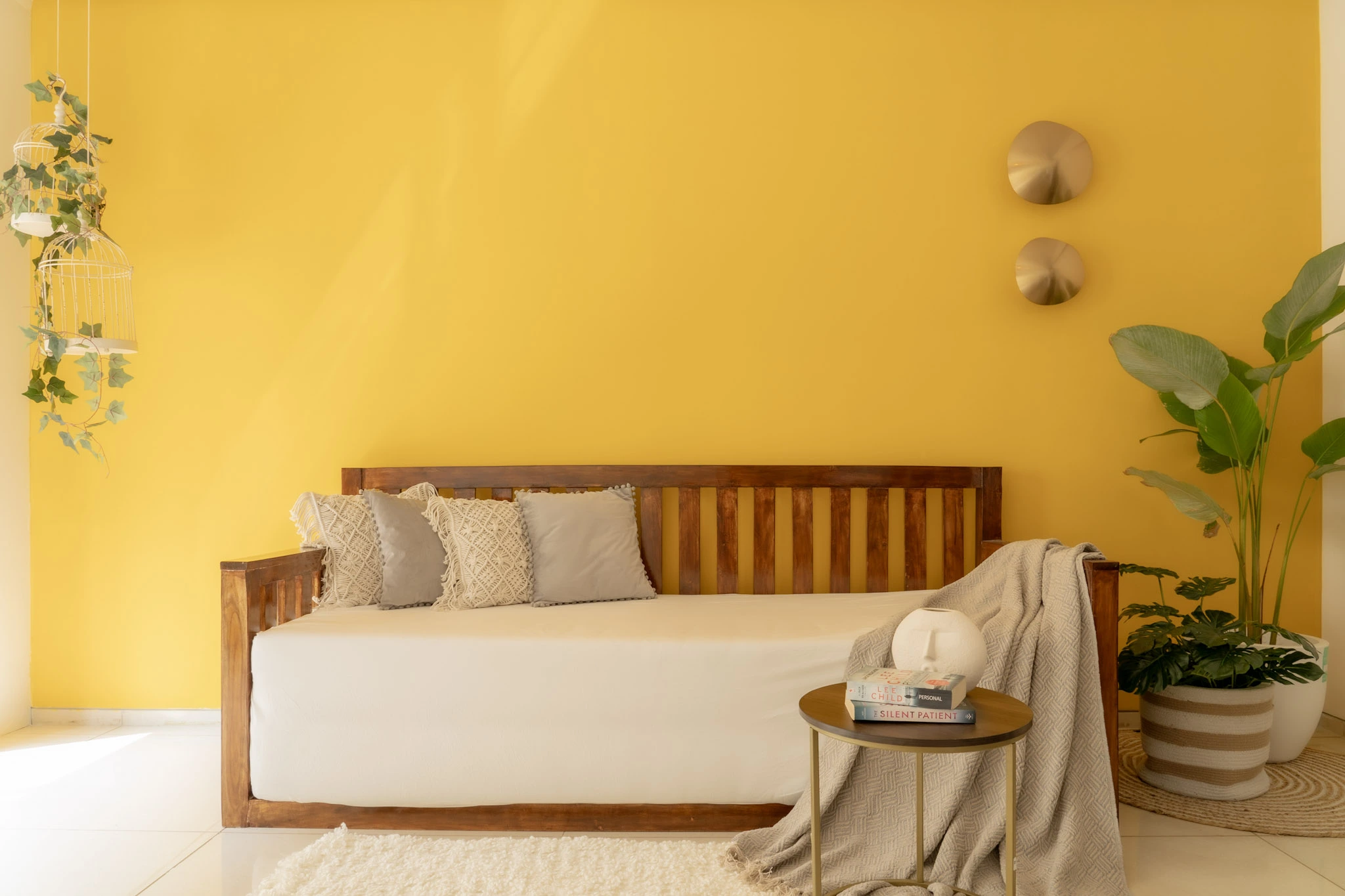 Cozy lounge seating area with yellow accent wall, wooden daybed, indoor plants, and natural light