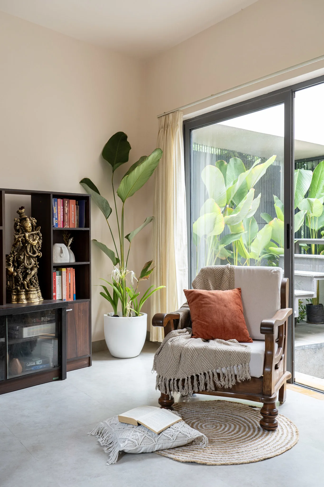 Cozy reading corner with wooden armchair, bookshelf and indoor plants near sliding window