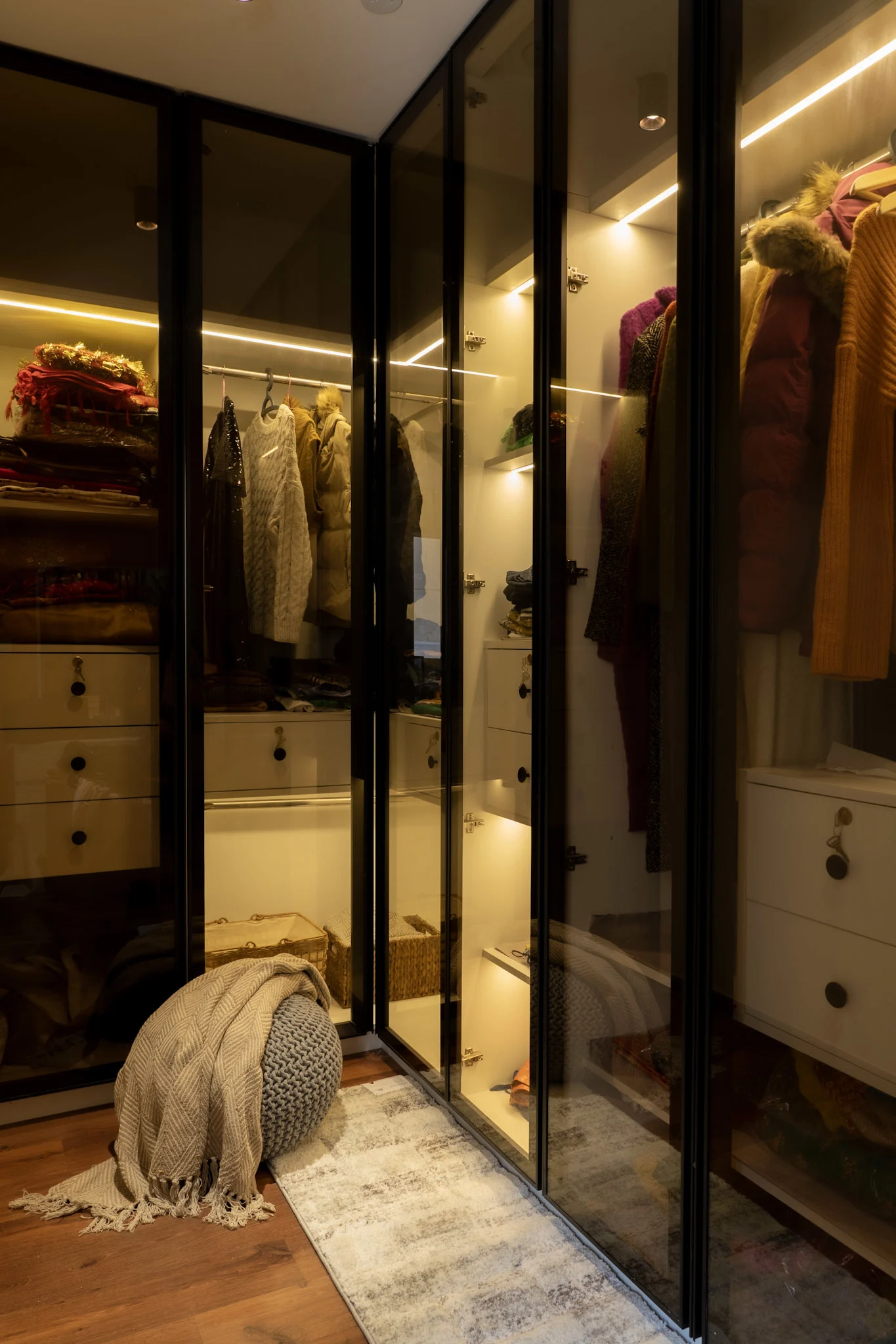 Modern walk-in wardrobe with glass shutters, warm lighting, and organized luxury storage space