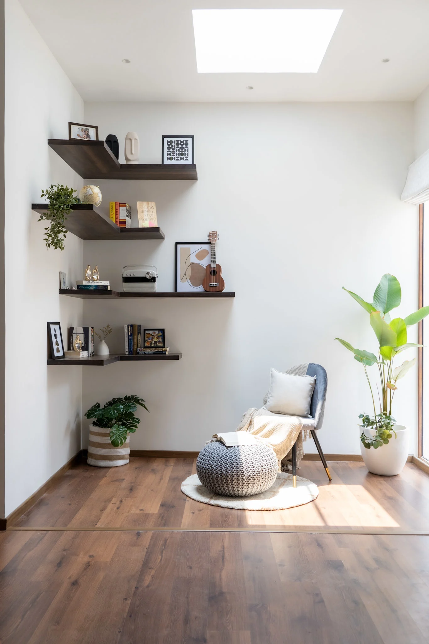 Cozy reading corner with floating wooden shelves, indoor plants, skylight, and modern chair