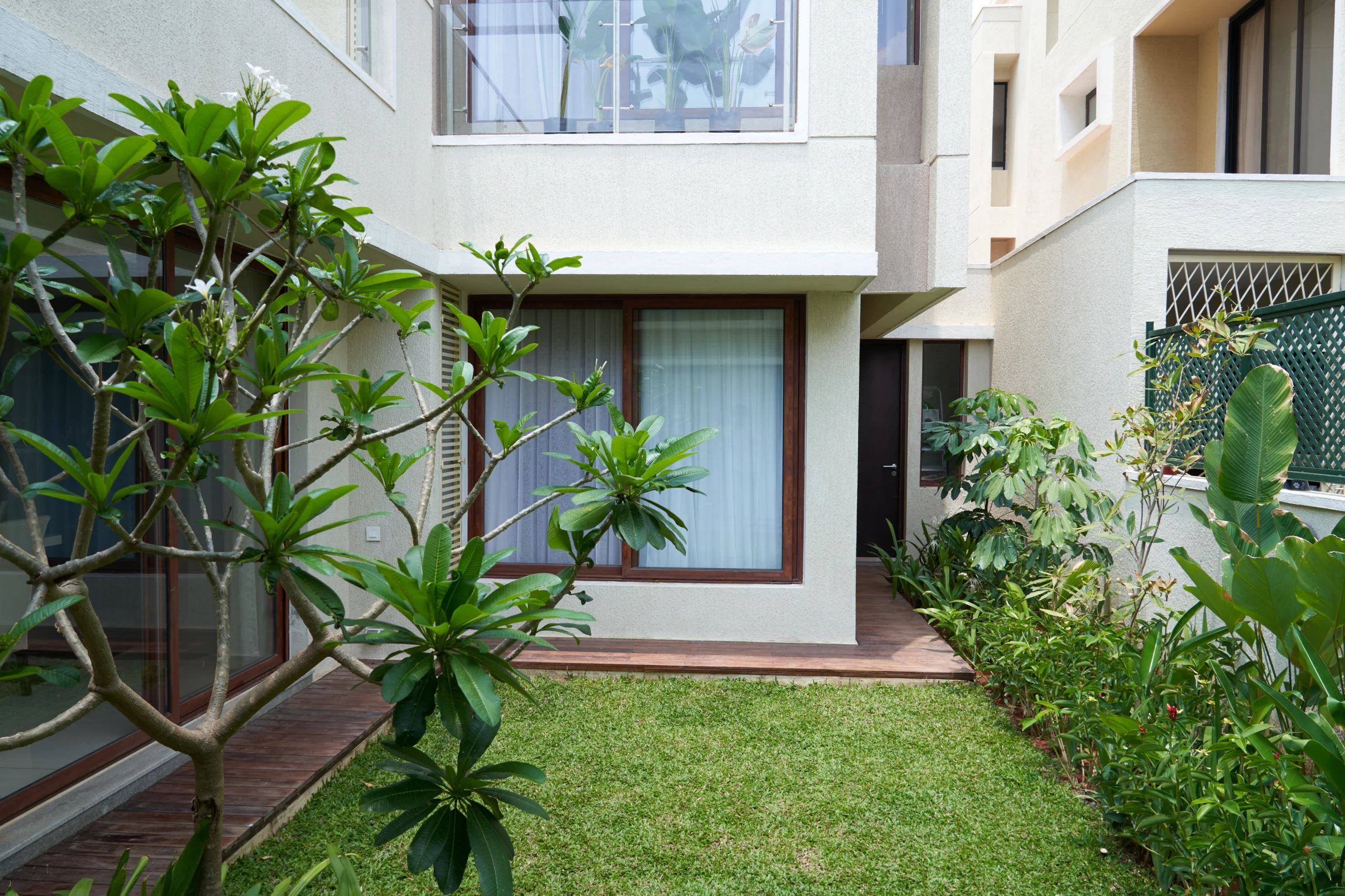 Modern villa courtyard landscape with green lawn, tropical plants, wooden deck flooring, and contemporary residential architecture in Bangalore