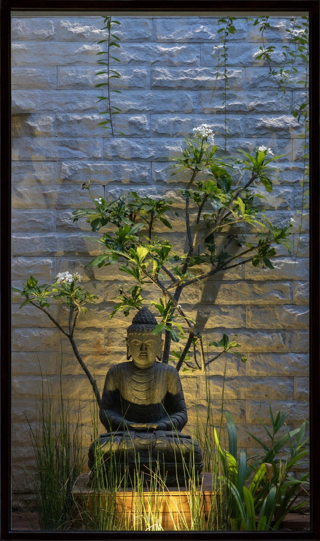 Buddha statue courtyard with natural stone wall, soft lighting, and tropical landscape design in luxury villa
